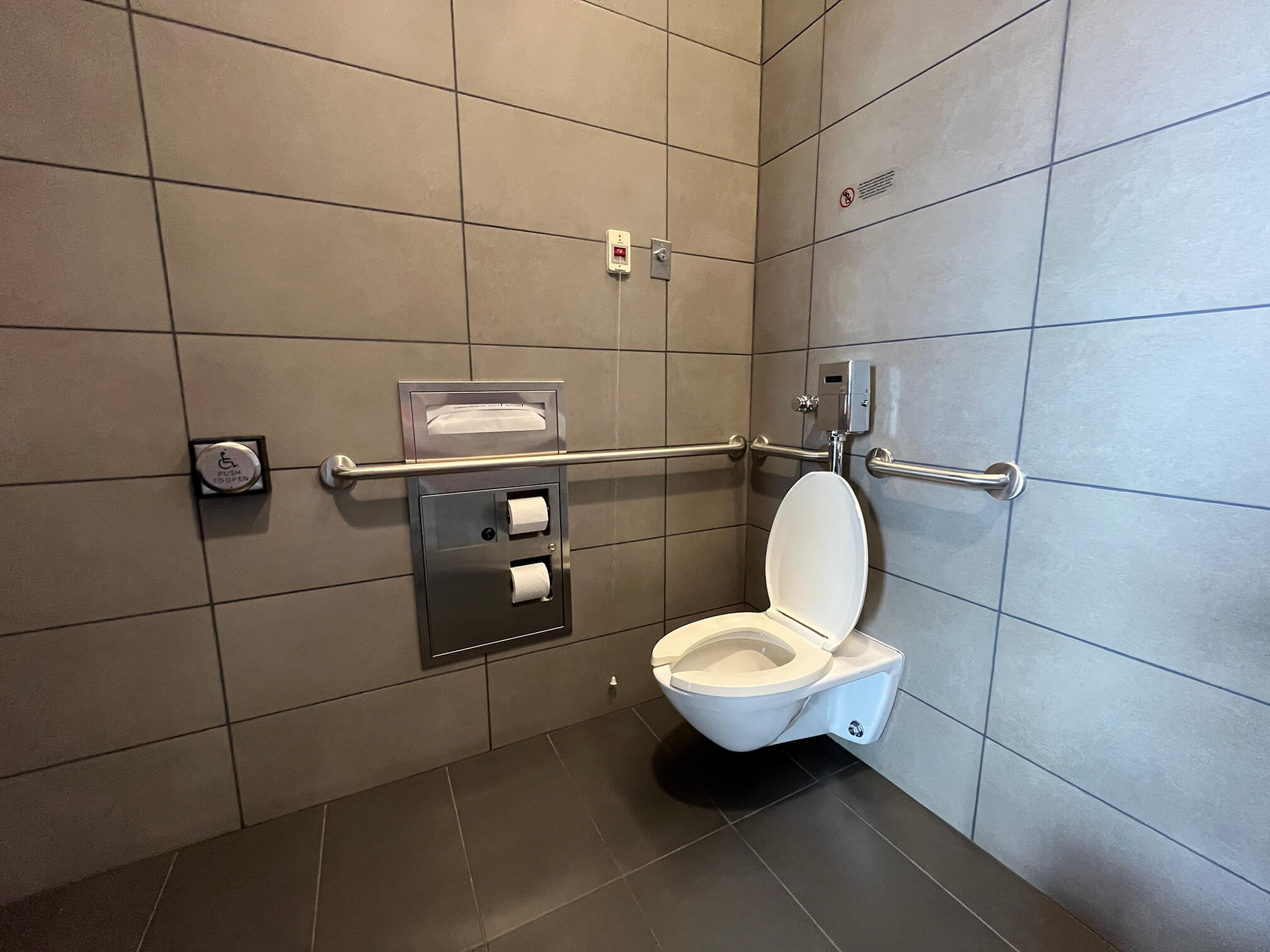 Typical universal restroom interior, with grab bars, power-operated door for the entrance, and emergency pull cord.
